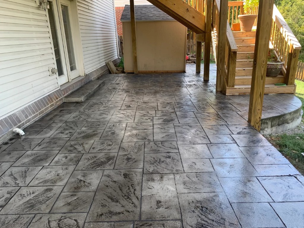 Stamped concrete patio under wood deck stairs