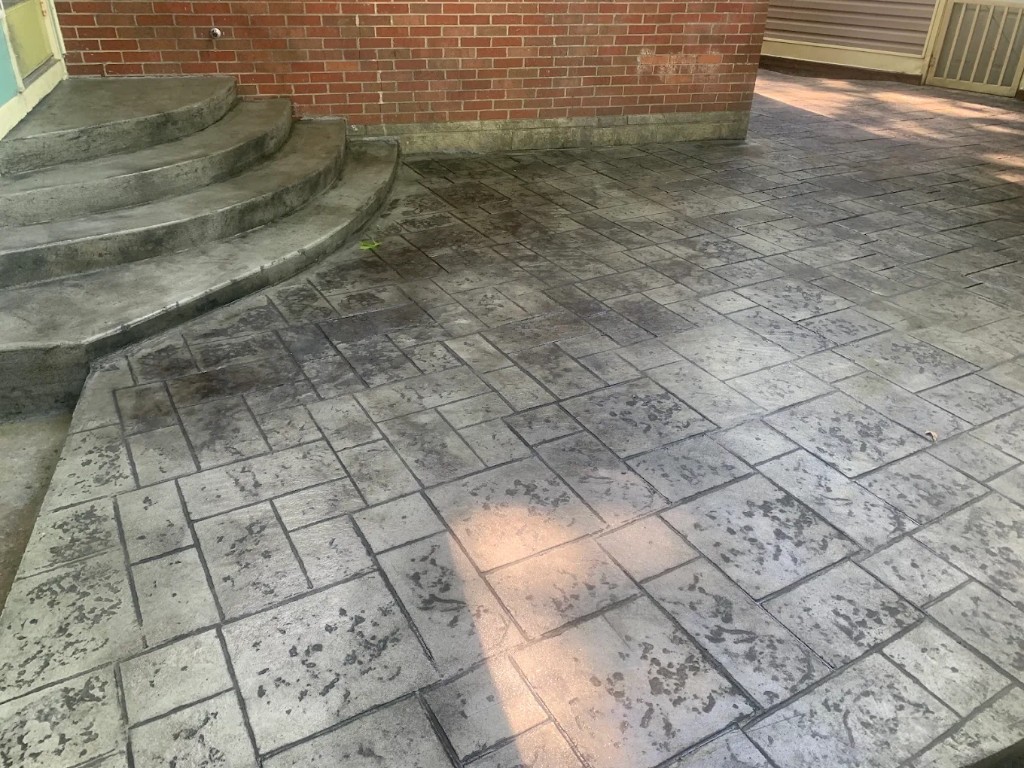 Stamped stone patio wrapping curved concrete steps against a brick wall