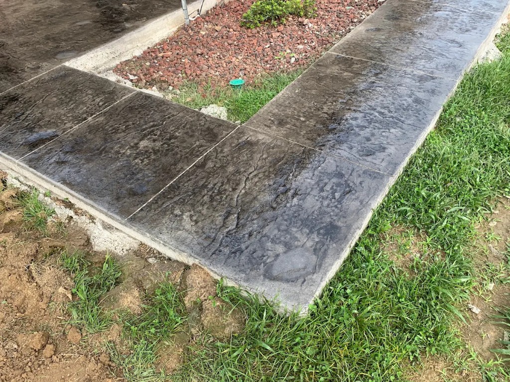 Dark stamped concrete walks meeting at a corner in the grass